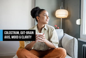 Woman sitting cross-legged on a sofa holding a mug and smiling contentedly, with text overlay reading Colostrum Gut-Brain Axis Mood and Clarity