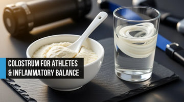 Ceramic bowl of ivory colostrum powder with a spoon on dark slate beside a glass of water with powder dissolving, foam roller and resistance band softly out of focus in the background