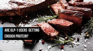 Cooked steak on a slate board with rosemary and peppercorns.